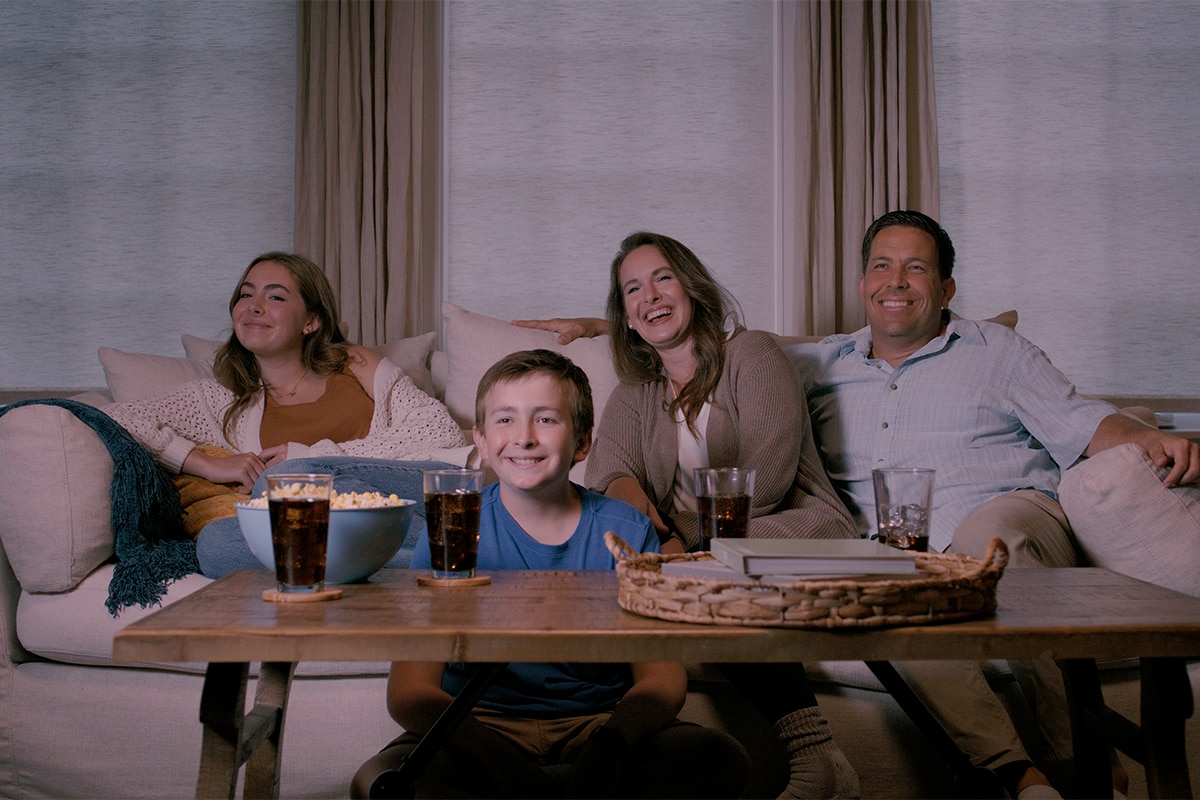 Family sitting on the couch watching a movie with blackout shades fully closed.