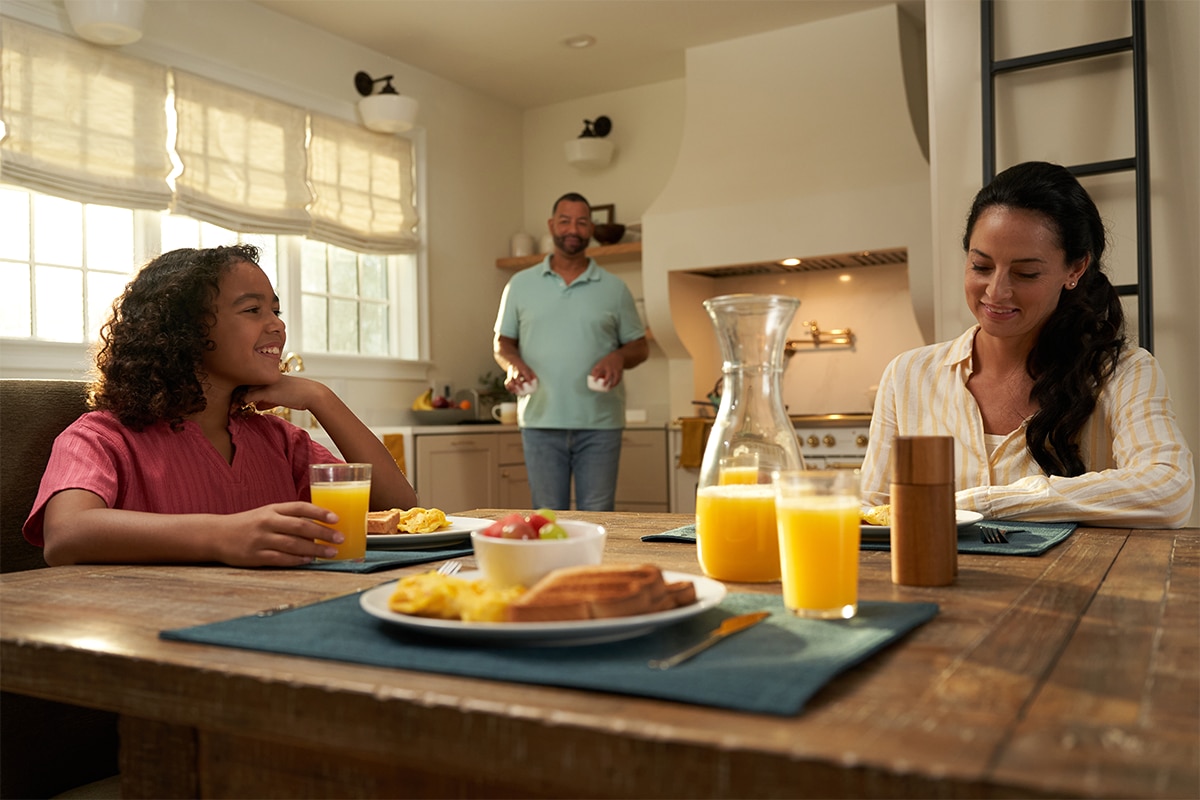 Family eating breakfast at the kitchen table as Roman shades open behind them.