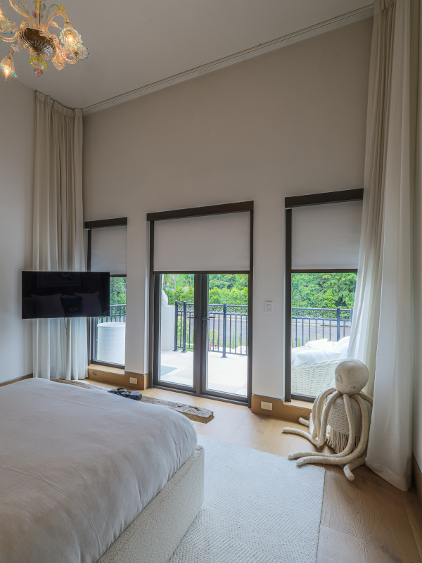 Modern bedroom, and an octopus plushy in the corner, with shades open overlooking a balcony with views of greenery.